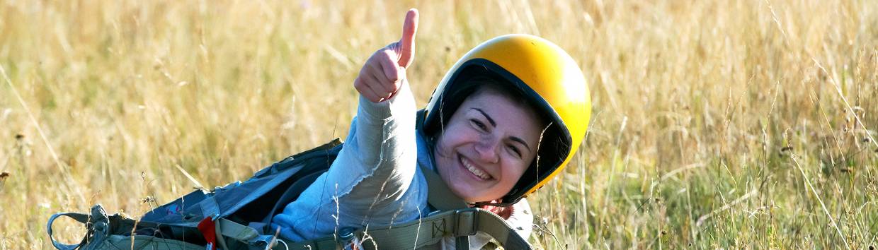 En leende kvinna med hjälm halvligger på en gräsmatta och gör tumme upp